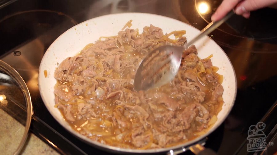 Large slotted spoon stirs beef, onion, sauce mixture in skillet while steam rises