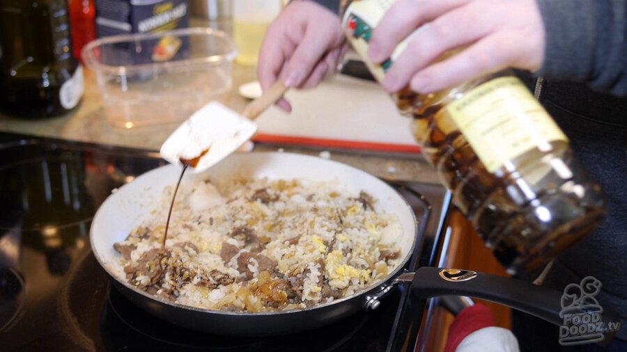 Using spatula to eventually distribute soy sauce throughout pan by pour sauce onto spatula and then moving it around in circles over pan