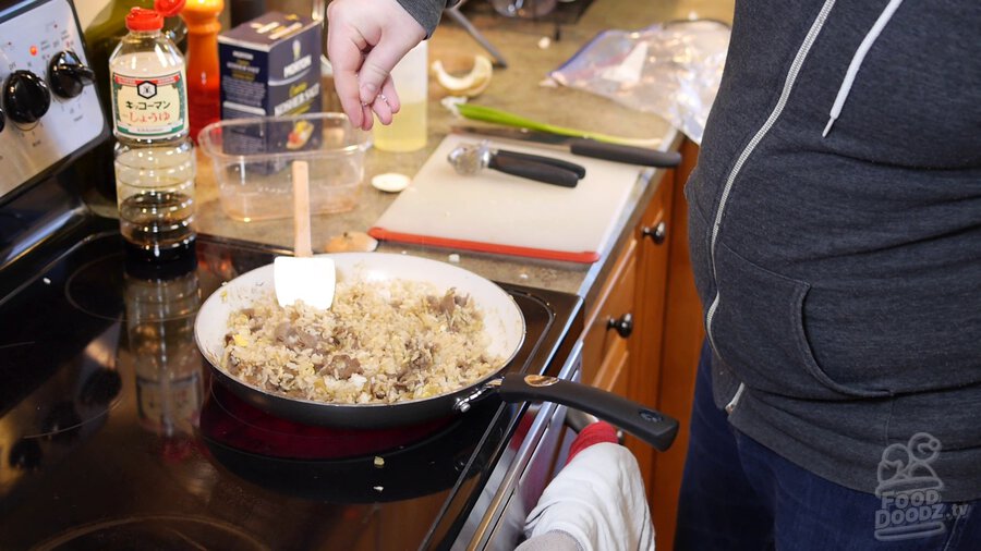 Completed pan of fried rice is seasoned with salt to taste