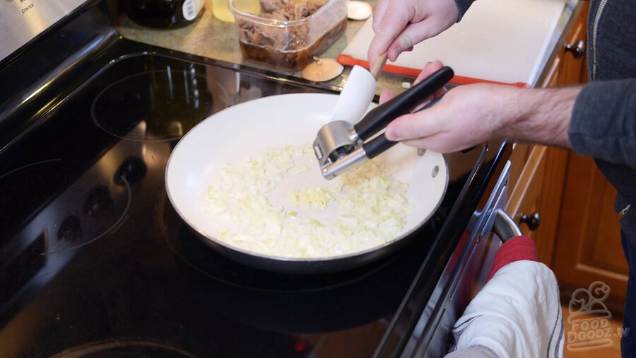 Garlic is minced in garlic press and added to pan