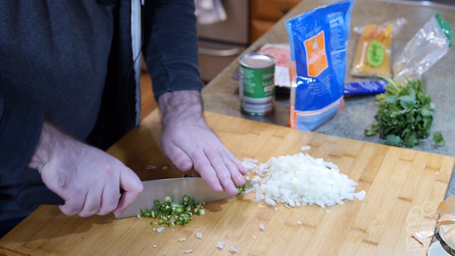 Onion and serrano pepper being chopped on wooded cutting board