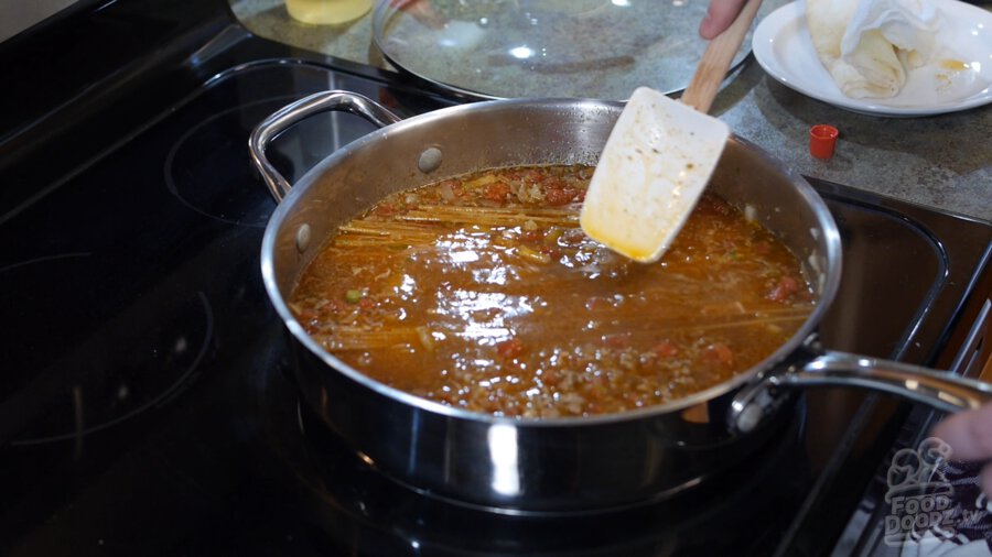 Large spoon is used to press spagetti below water level in pan to ensure it cooks