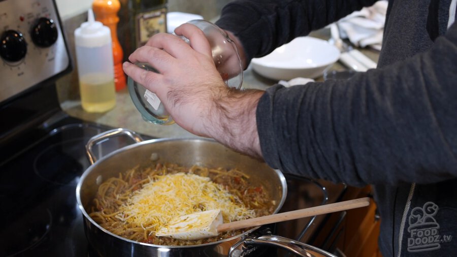 Grated cheese is added to taco spaghetti pan from measuring cup