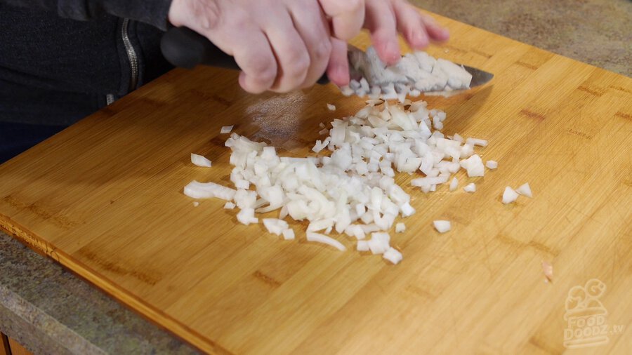 Onion is chopped with chef's knife on wooden cutting board