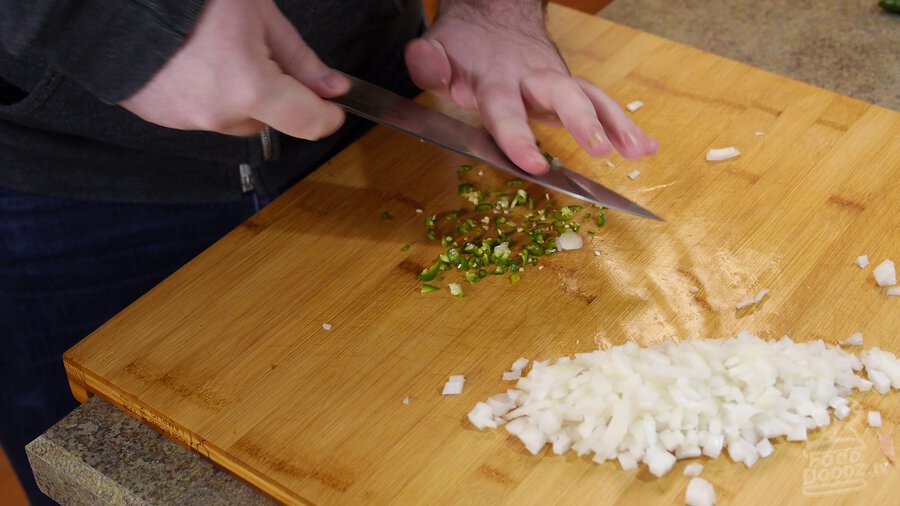 Serrano is chopped with chef's knife on wood cutting board