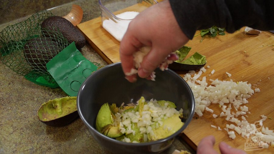 Adding onion and serrano peppers to bowl of avocado chunks.