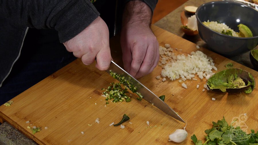 Using chef's knife to mince serrano peppers. Chopped onion can be seen in background.