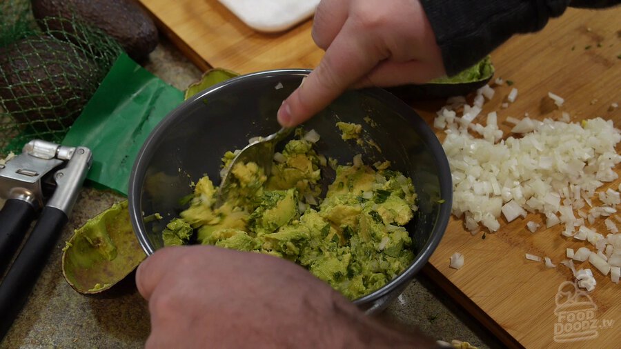 Using spoon to mash avocado and incorporate onion, serrano, and cilantro mixture.