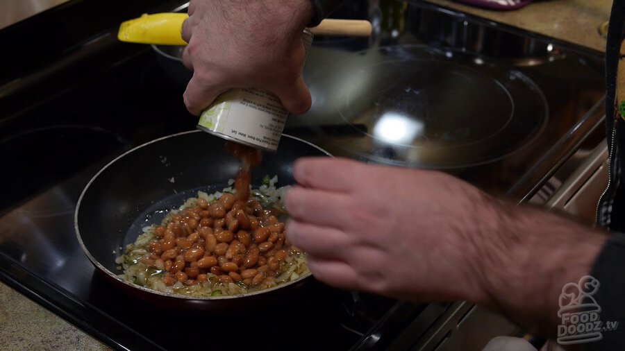 Can of pinto beans is added to skillet with onions and serrano peppers