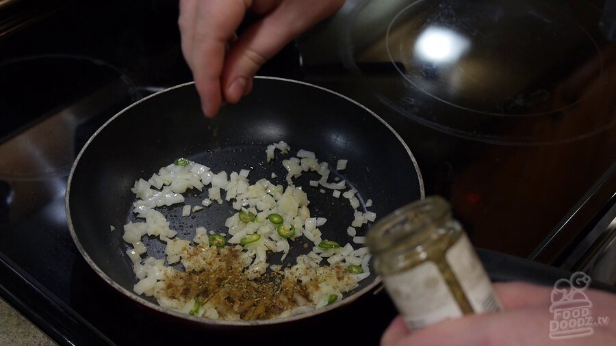 Cumin and oregano are added to skillet with onions and serrano peppers