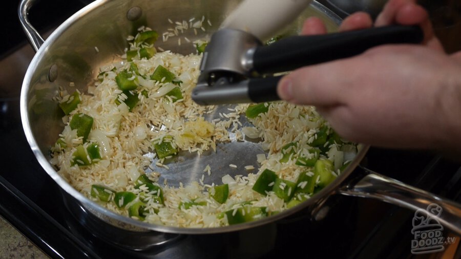 Garlic press is used to mince garlic and add to pan of toasted rice