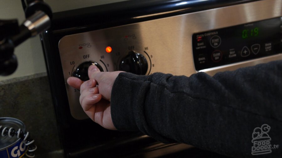 Hand turns knob of stove to low setting