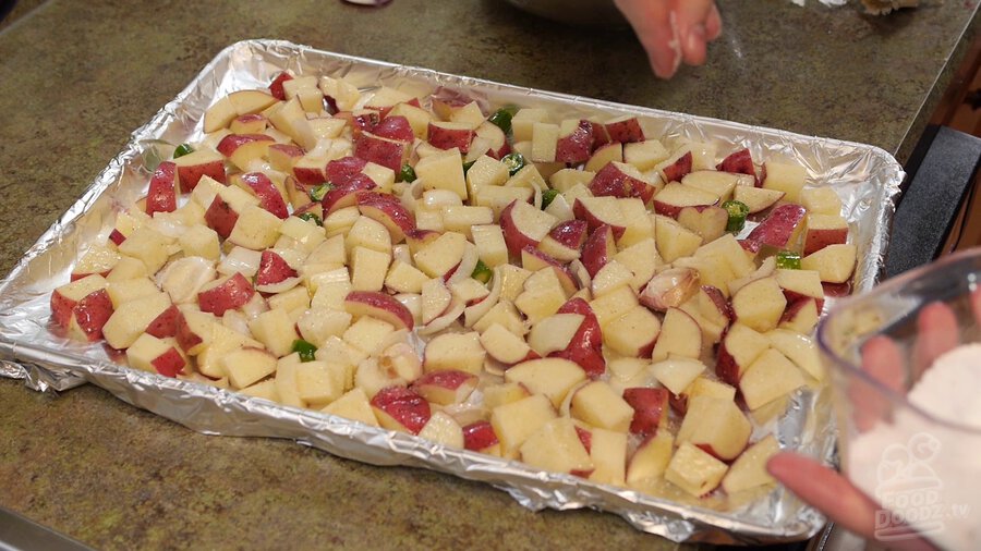 Sprinkling salt all over baking sheet to fully coat potatoes, serrano peppers, and onions