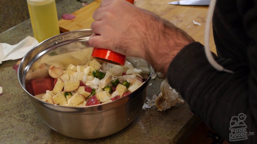 Turning pepper grinder to add fresh cracked pepper to bowl of chopped/chunked potatoes, serrano peppers, and onions