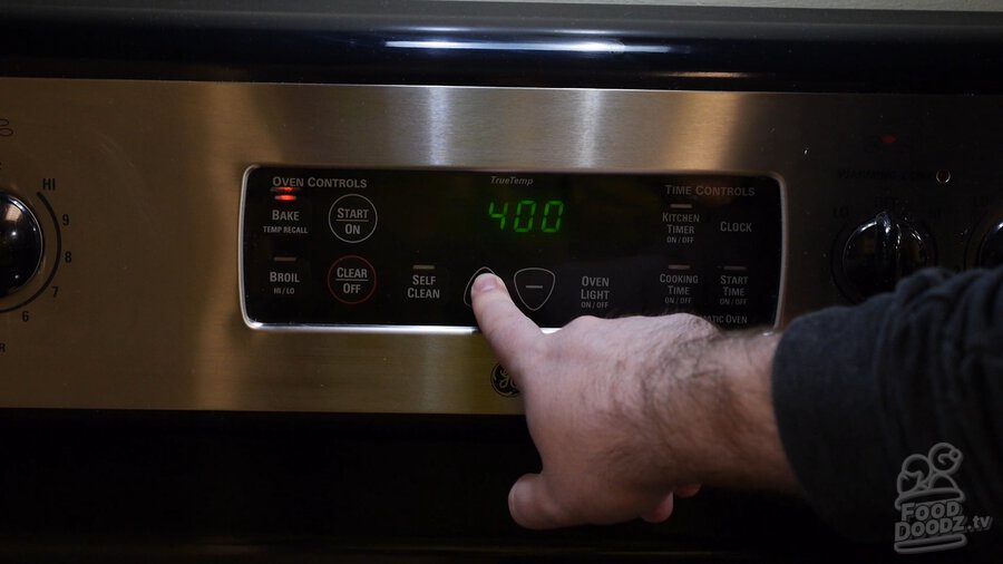 Hand presses button on oven control panel setting it to 400 degrees