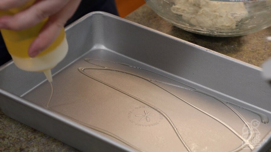 Using squirt bottle to add vegetable oil to inside of baking sheet pan