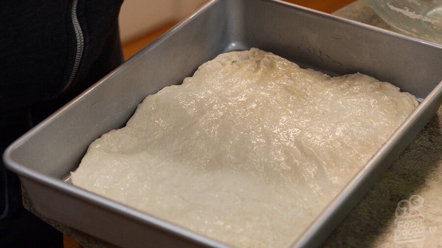 Pizza dough stretched and flattened into greased sheet pan