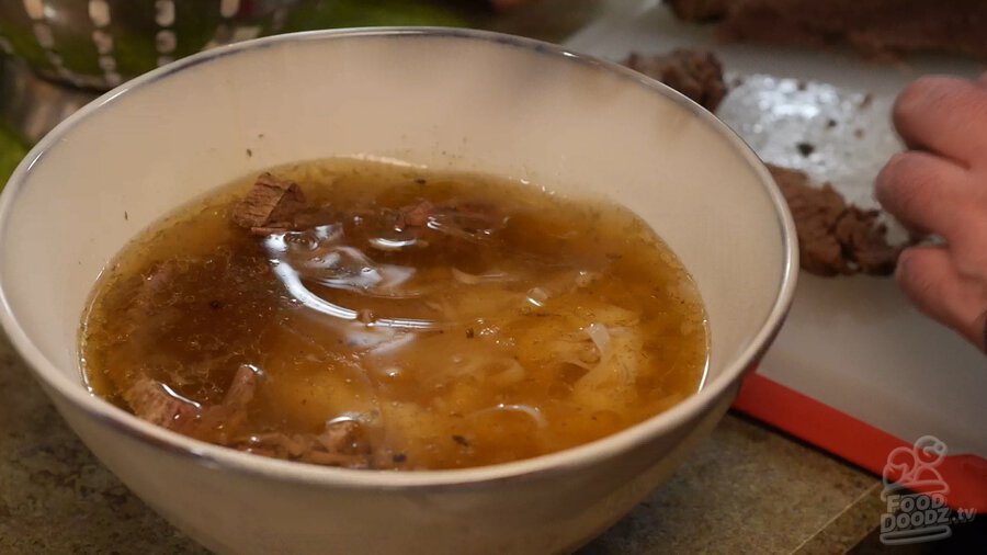 Sliced beef brisket placed in bottom of bowl with noodles and broth added on top