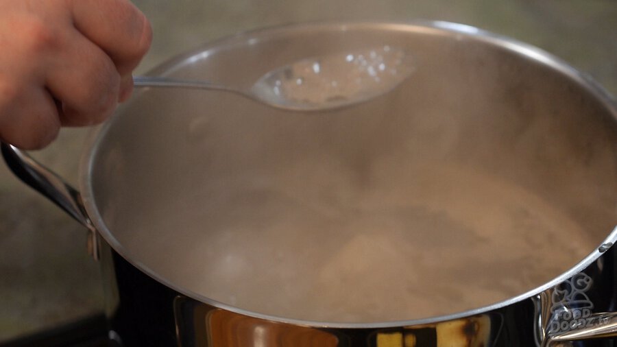 Using spoon to skim top of boiling beef bone broth for Vietnamese pho