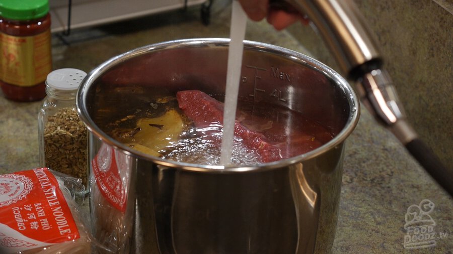 Filling Instant Pot with water to cover beef brisket, bones, spices for Vietnamese pho