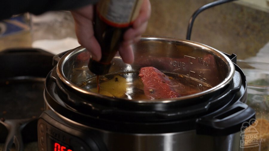 Shaking fish sauce bottle over instant pot to add fish sauce to Vietnamese Pho