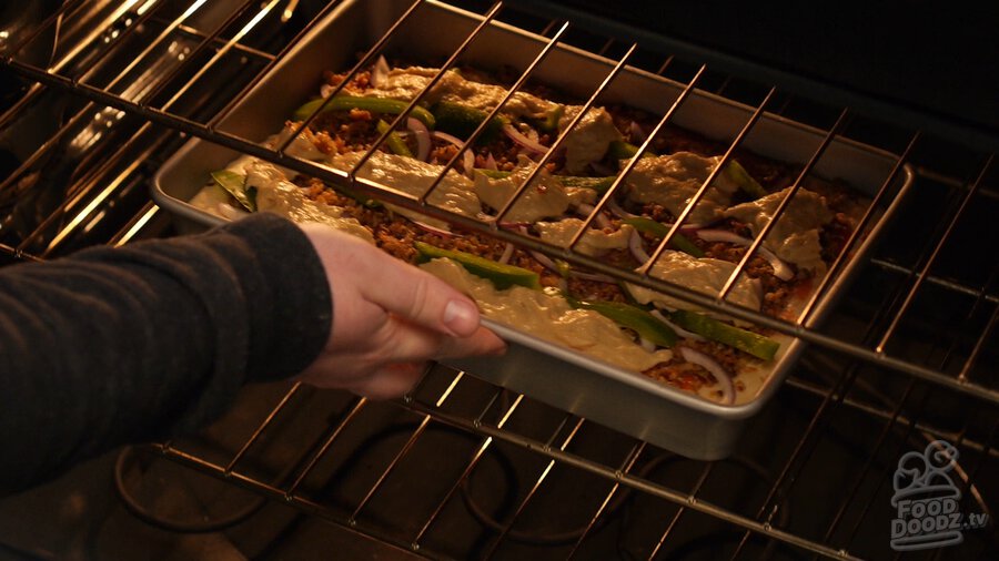 Hand places sheet pan pizza on rack in oven