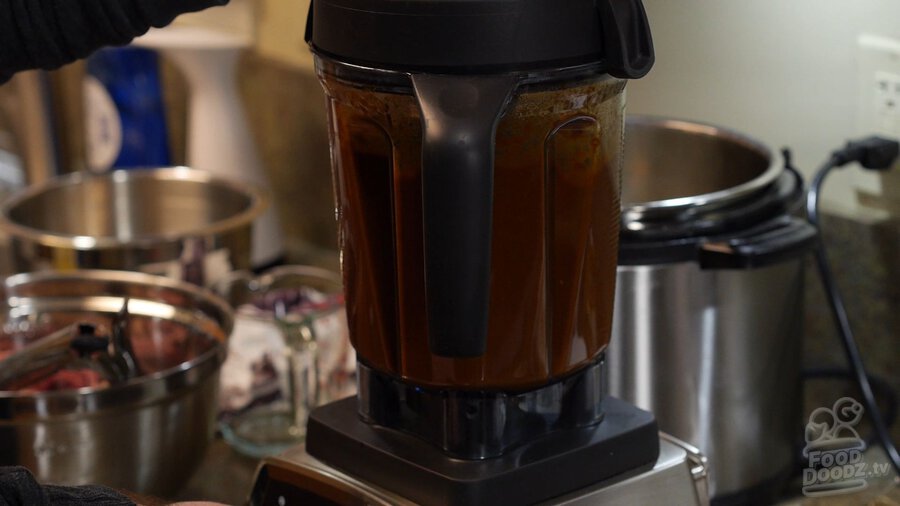 Chili mixture being blended in blender with hand holding lid on