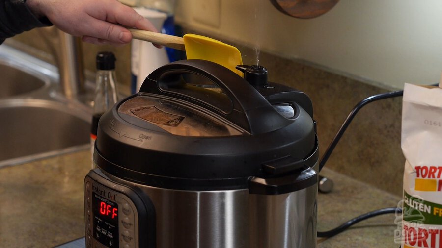 Hand uses spoonula to release pressure valve on Instant Pot