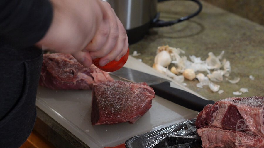 Seasoning chunks of chuck roast beef with salt and pepper