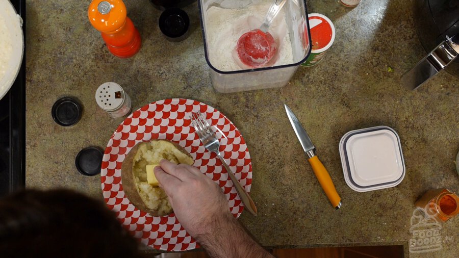 Butter being put on top of salted and peppered baked potato