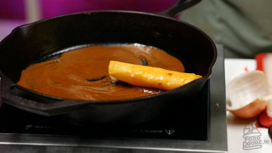 Placing the rolled, filled tortilla into the sauced pan