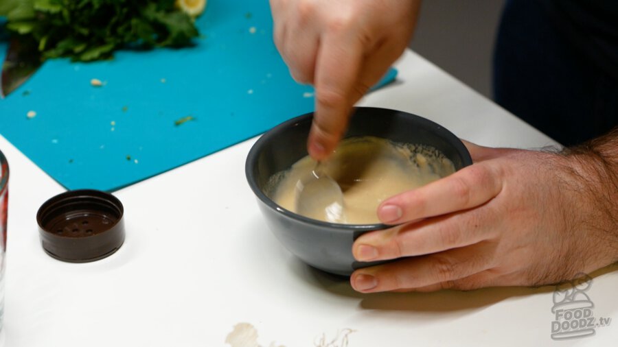 Mixing the tahini sauce together well to get it well emulsified.