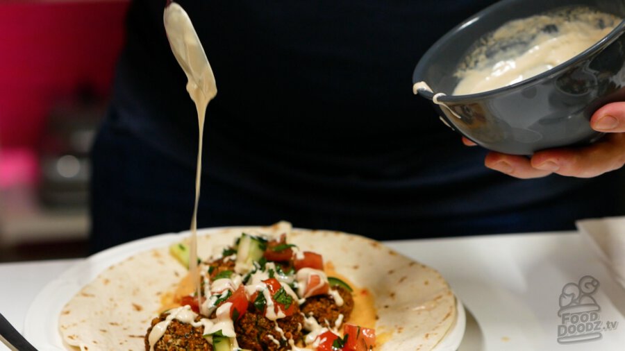 Drizzling tahini sauce over the top